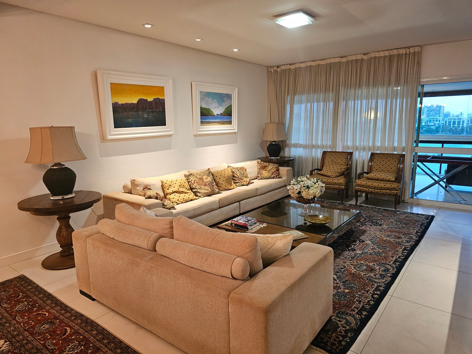 Sala de estar com sofá bege, tapete persa e quadros na parede